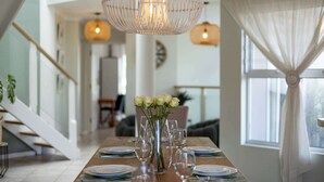 A dining area with a wooden table set for six, a vase of white roses, and hanging pendant lights. - Beachfront Villa Sea Breeze ,hout Bay (Cape Town)