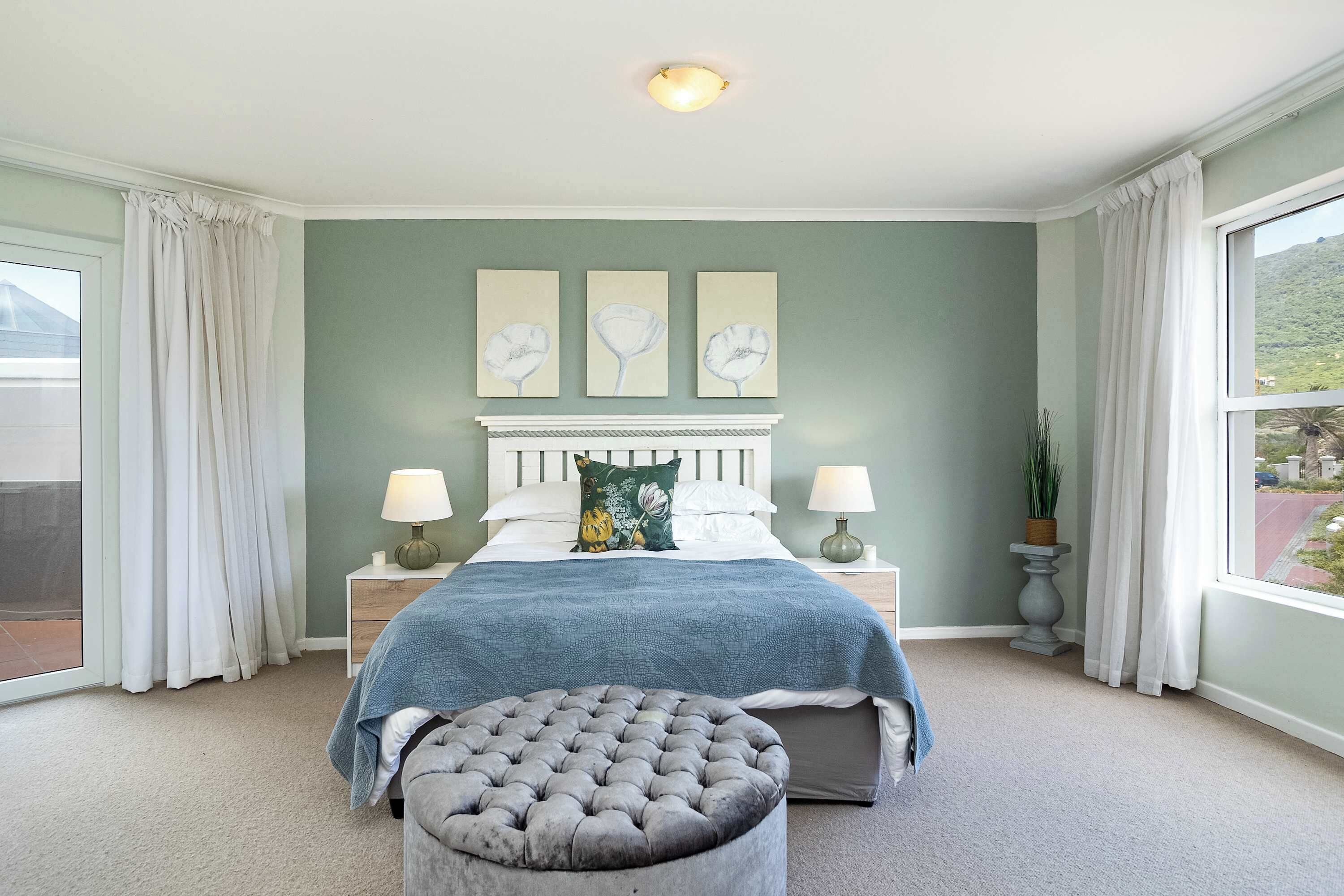 A bedroom with a bed, two bedside tables, a window with curtains, and a view of a mountain.