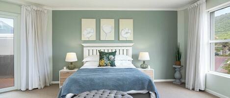 A bedroom with a bed, two bedside tables, a window with curtains, and a view of a mountain.