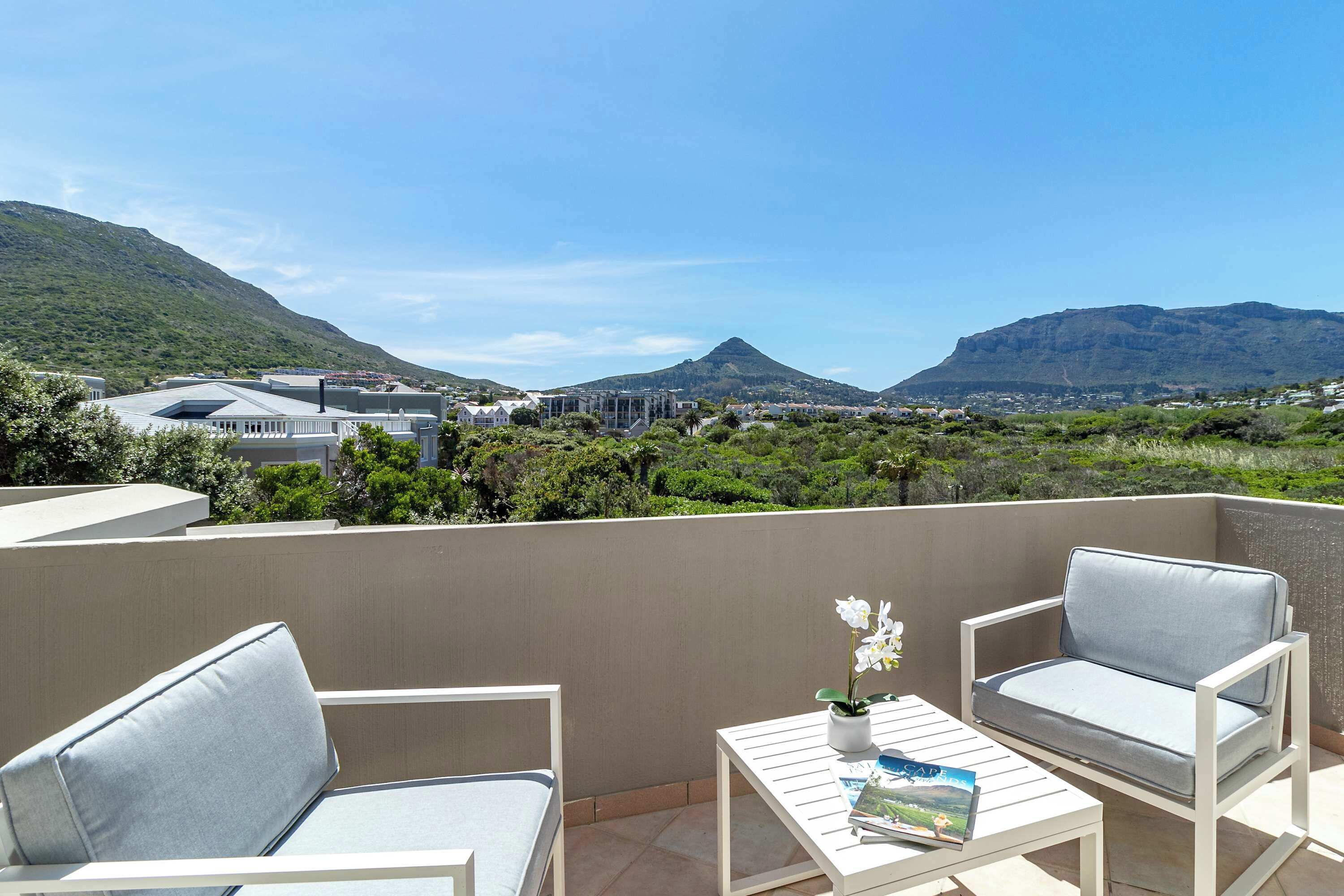 A balcony with two white chairs and a small table, overlooking a mountainous landscape with buildings in the background.