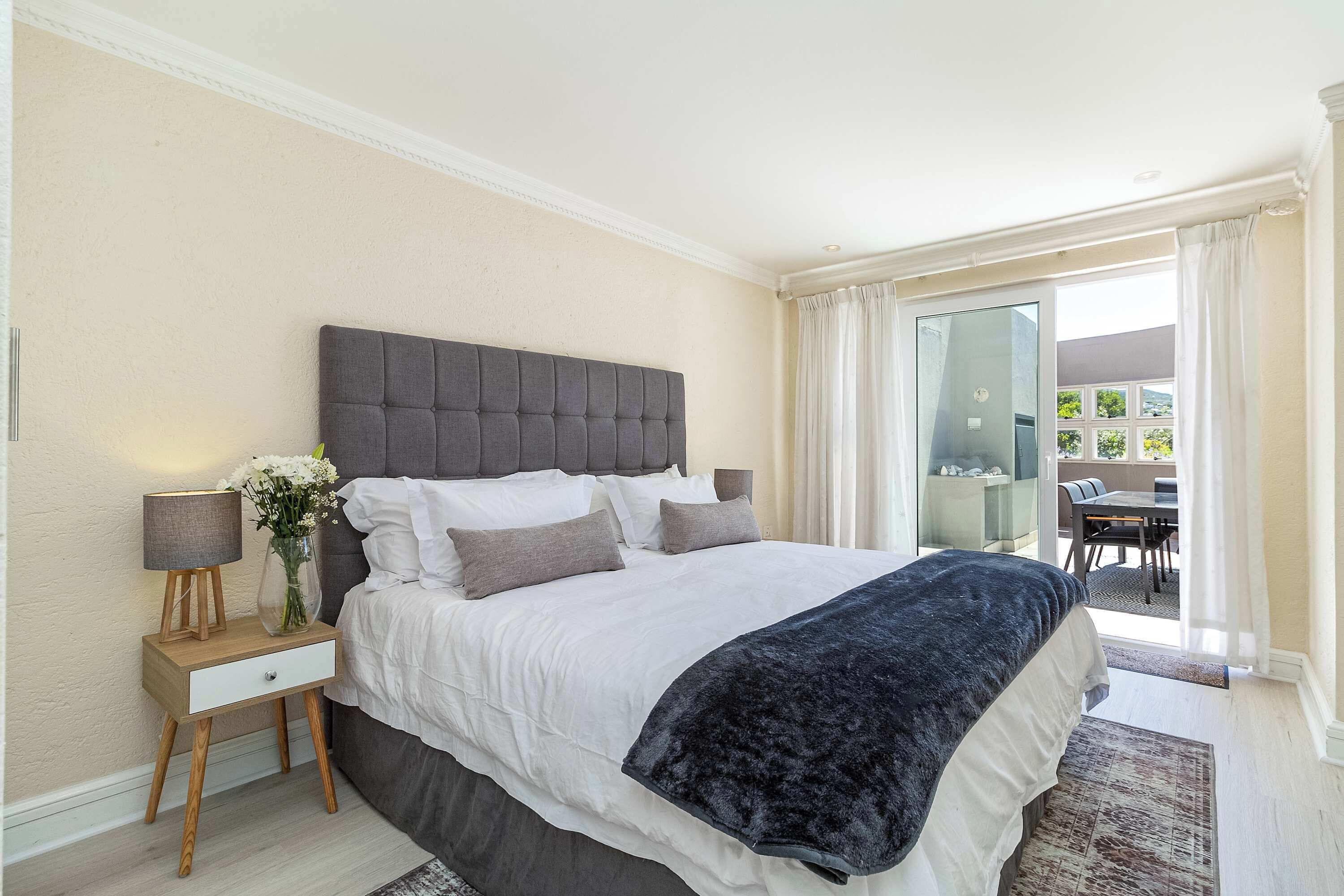 A bedroom with a large bed, a bedside table with a lamp, and a view of the outside balcony.
