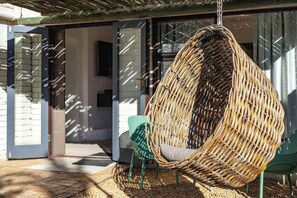 A wicker hanging chair with a cushion, green chairs, and a glass door leading to an interior space.
