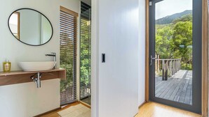 A modern bathroom with a large oval mirror, a white vessel sink, and a wooden vanity. - Luxury Eco Haven With Garden Cottage - Hout Bay (Cape Town)