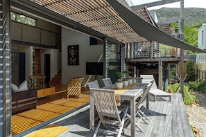 A modern outdoor deck with wooden furniture, a dining table, and potted plants. - Luxury Eco Haven With Garden Cottage - Hout Bay (Cape Town)