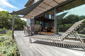 A wooden deck with outdoor furniture, a pergola, and a glass wall reflecting the surrounding landscape. - Luxury Eco Haven With Garden Cottage - Hout Bay (Cape Town)