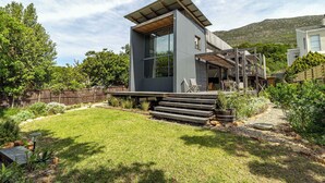 A modern house with a large glass window, a wooden deck, and a stone pathway. - Luxury Eco Haven With Garden Cottage - Hout Bay (Cape Town)