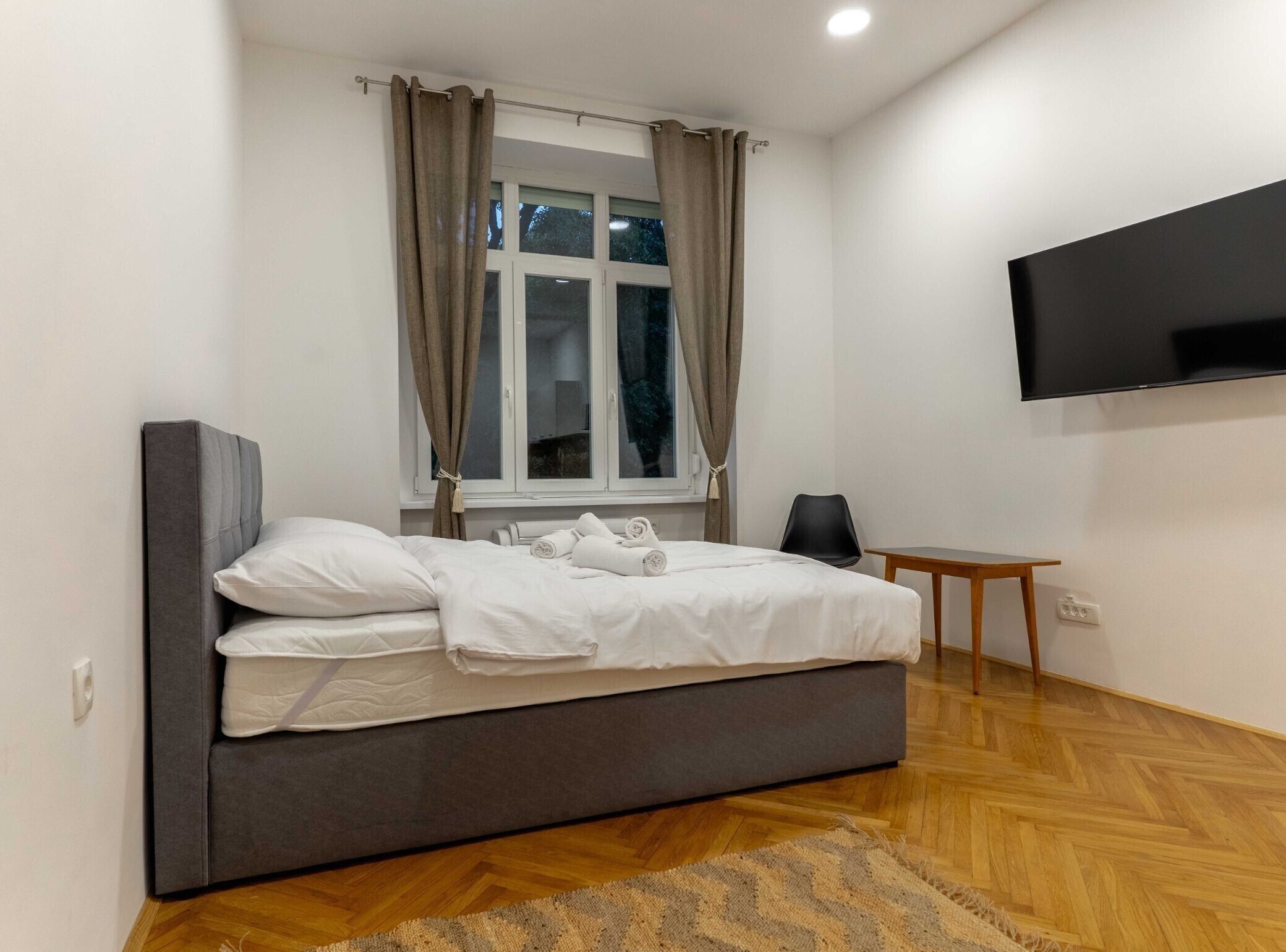 Une chambre moderne avec un grand lit, une petite table, une chaise et un téléviseur fixé au mur.