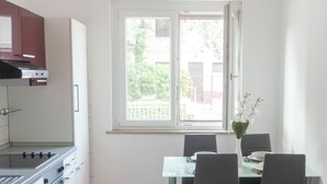 Eine moderne Küche mit Gasherd, Mikrowelle und integriertem Backofen. Ein Esstisch mit Stühlen und eine Blumenvase sind vorhanden. Ein Fenster bietet einen Blick nach draußen.