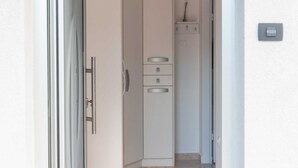 Ein schmaler Flur mit einer Tür links, einem weißen Schrank mit Schubladen in der Mitte und einem kleinen Regal mit einer Vase rechts.