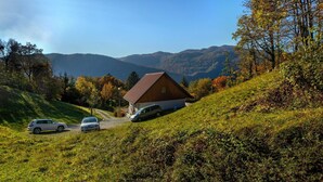Une maison avec un toit en pente, située sur une colline, entourée d’arbres et sous un ciel dégagé.