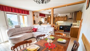 Un salon moderne avec un canapé, une table à manger pour quatre personnes et une cuisine en arrière-plan.