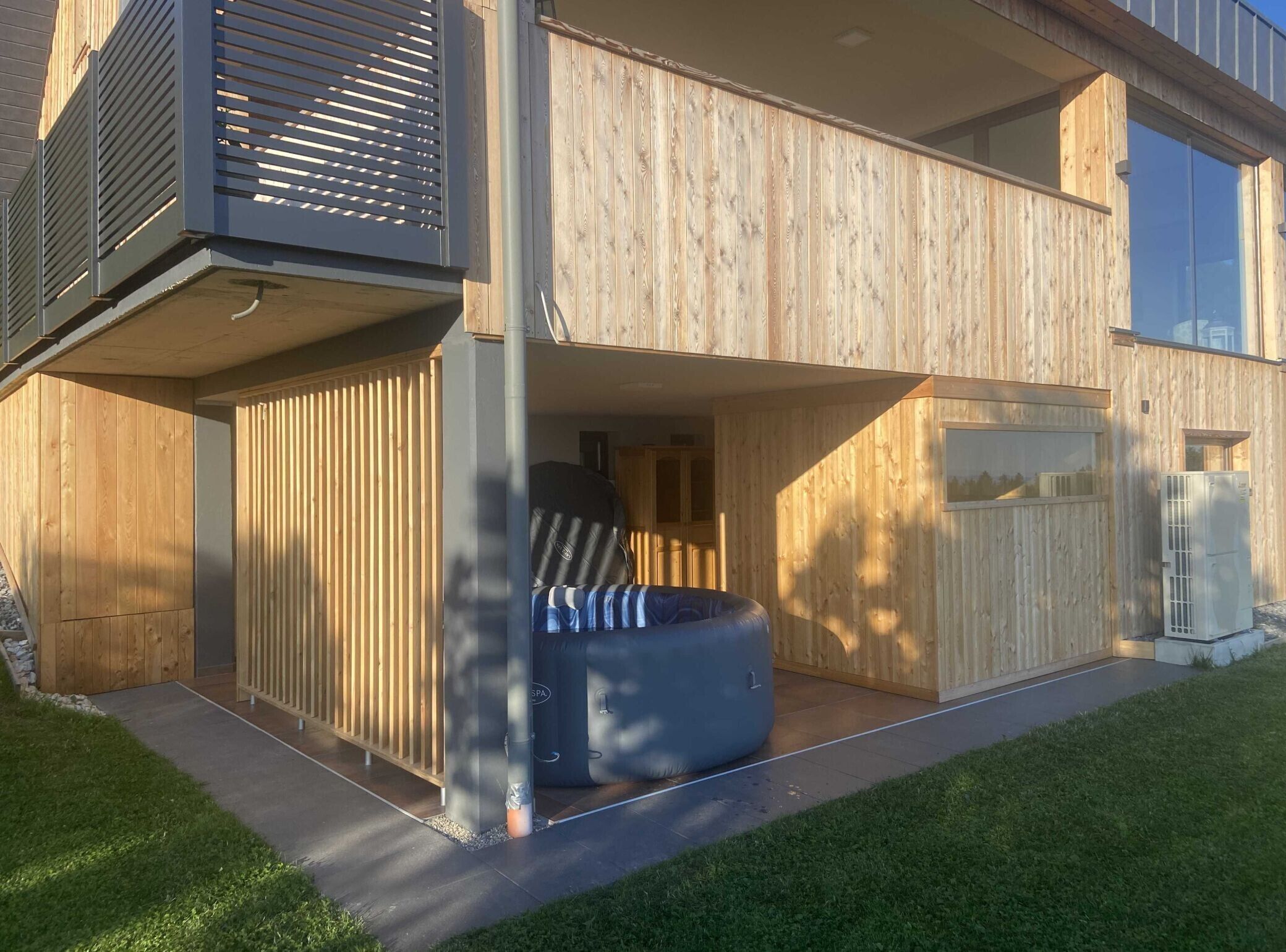 Un moderno edificio de dos plantas con fachada de madera, un jacuzzi y un amplio ventanal en el piso superior.