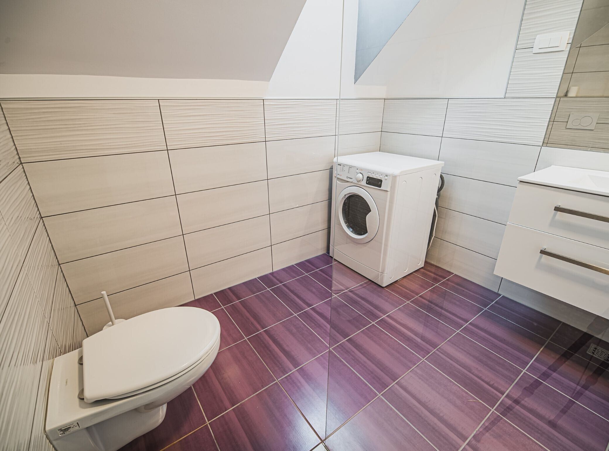 A compact bathroom with a washing machine, a toilet, and a small cabinet.