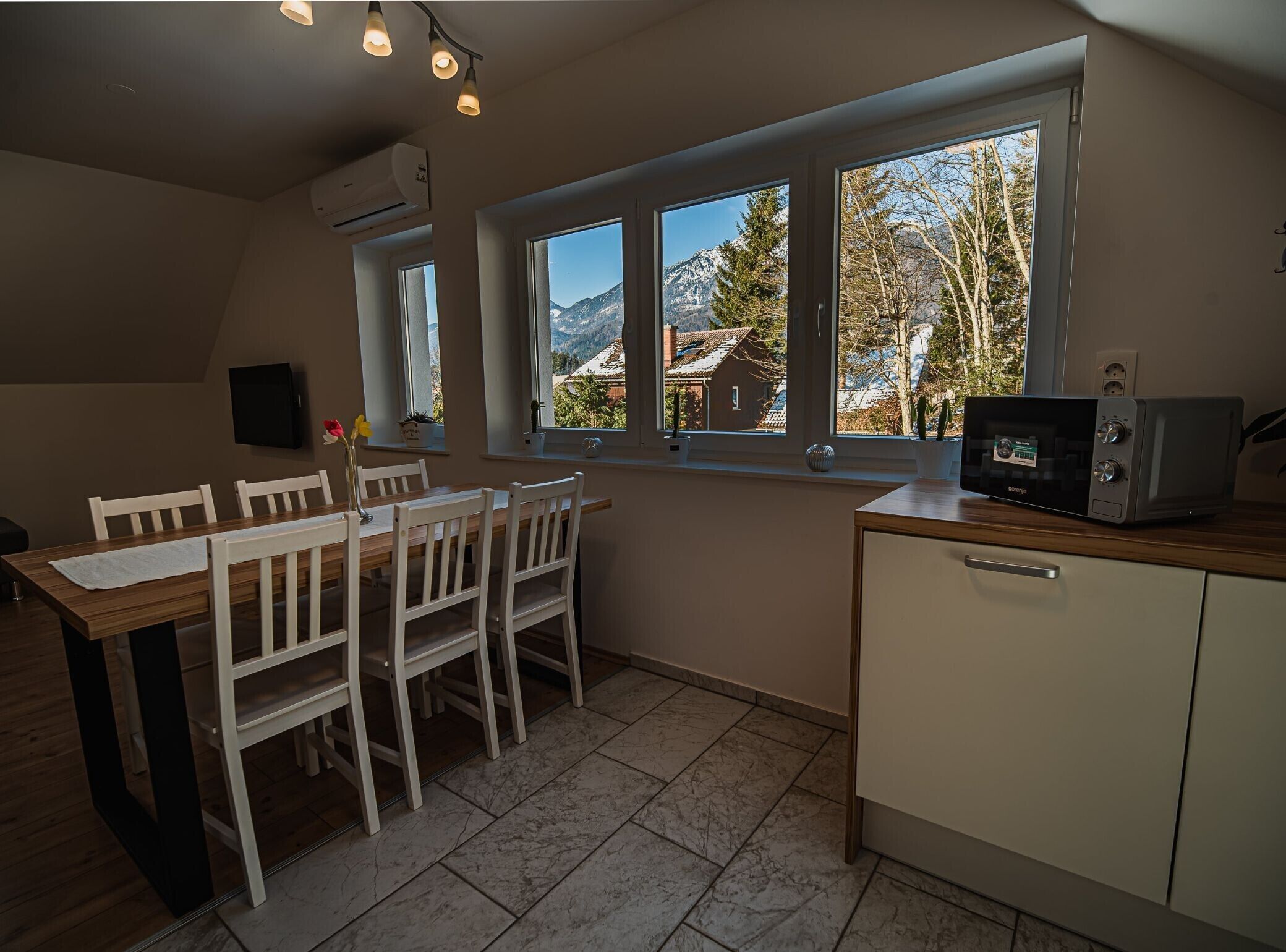 A kitchen with a dining table, chairs, a microwave, and a view of mountains through large windows.