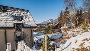 Una casa cubierta de nieve con un balcón, una montaña al fondo y cielo despejado.