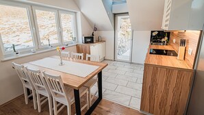 Una cocina moderna con una mesa y sillas de madera, horno empotrado y vistas al exterior a través de amplios ventanales.