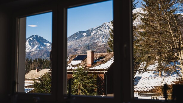 Vista a través de una ventana de un paisaje montañoso con tejados nevados y cielo despejado.