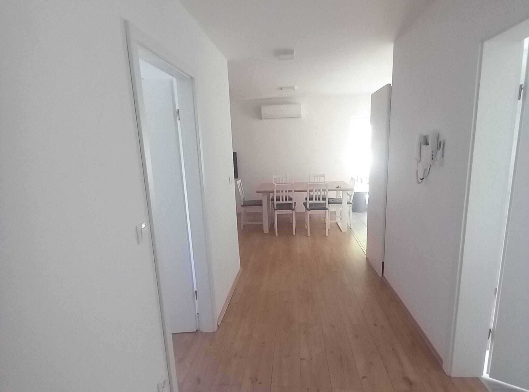 A hallway with wooden flooring leading to a dining area with white chairs and a table.