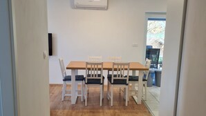 A dining area with a wooden table and four white chairs, an air conditioning unit on the wall, and a view of the outdoors through a glass door. - Idyllic and Charming Apartments with Terrace - Standard Two Bedroom Apartment with terrace (Preddvor)