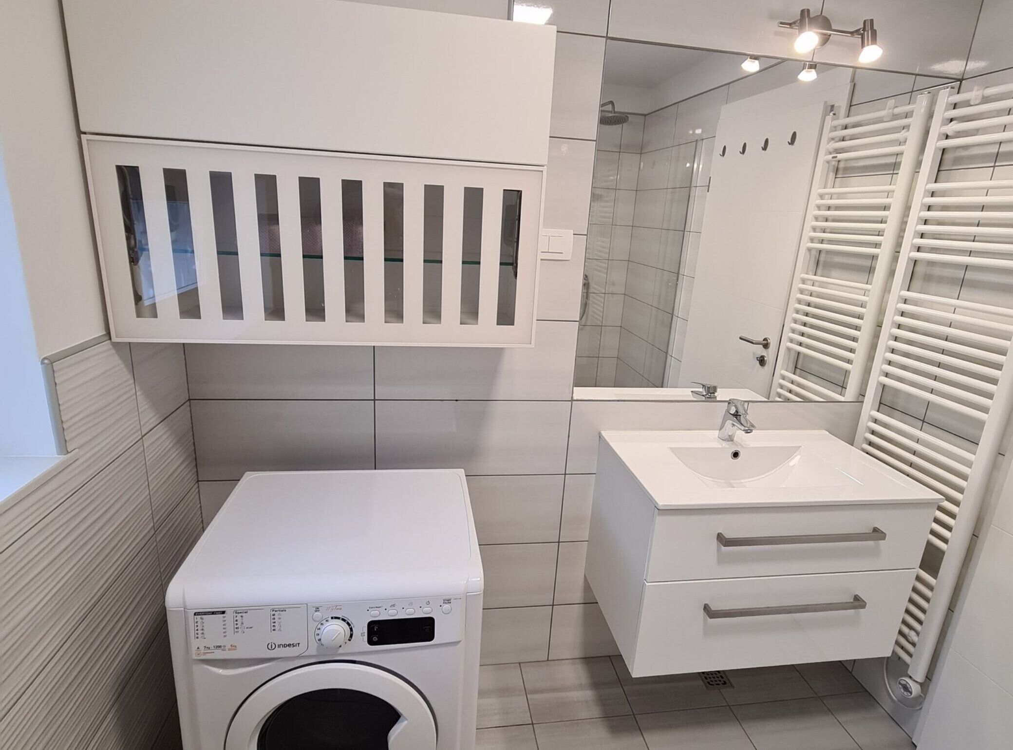 Ett modernt badrum med en inbyggd tvättmaskin, ett handfat och en duschhörna.
