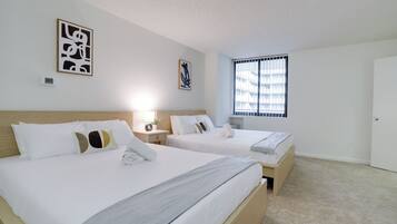 A hotel room with two beds, a window with blinds, and artwork on the walls.