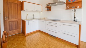 Une cuisine de taille réduite avec des meubles blancs, une porte en bois, un évier en acier inoxydable et une cuisinière intégrée.