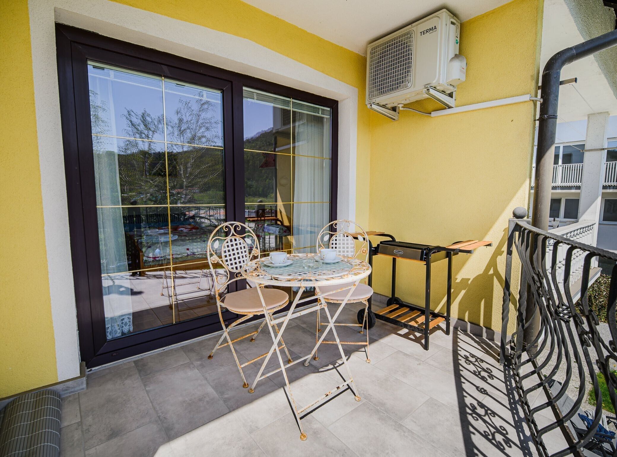 A balcony with a table and chairs, a window, and an air conditioning unit.