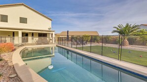Una piscina con barrera de vidrio, un patio cubierto y un césped bien cuidado con una palmera.