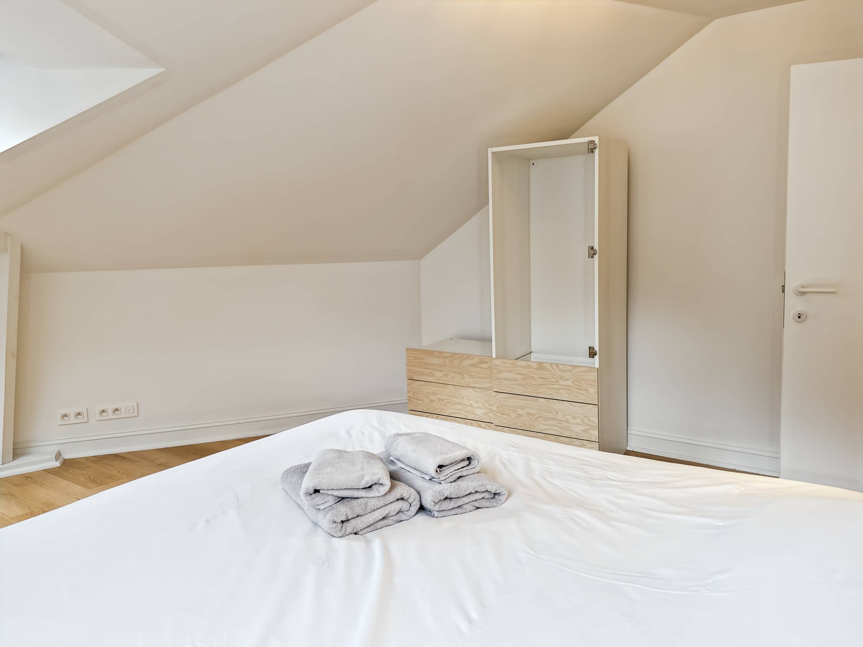 Une chambre avec un grand lit, un plancher en bois, un plafond blanc et une porte.
