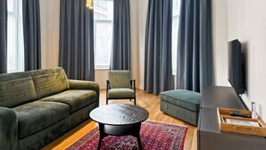 Ein modernes Wohnzimmer mit einem grünen Sofa, einem grünen Sessel, einem runden Couchtisch und einem an der Wand montierten Flachbildfernseher.