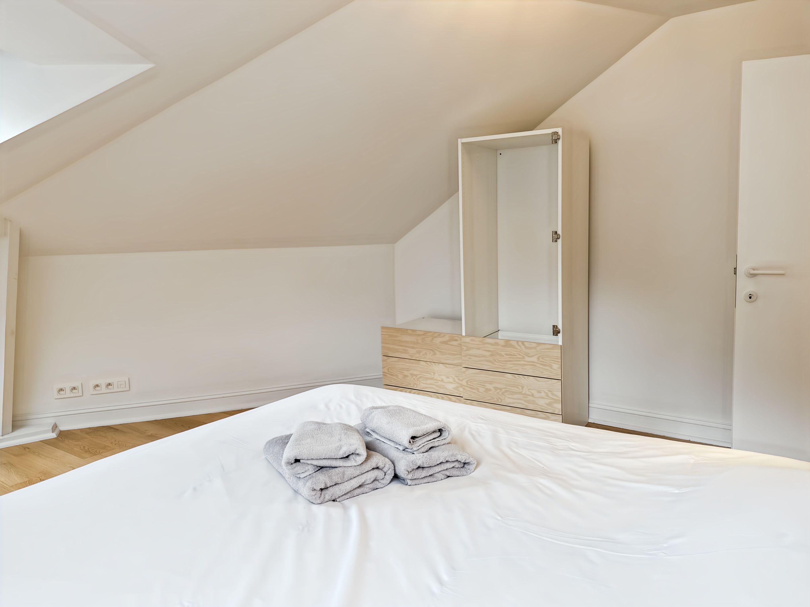 A bedroom with a bed, a wooden floor, a white door, and a mirror.