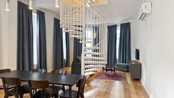 Un salon moderne avec un escalier en colimaçon, un coin repas avec une table et des chaises en bois, et un canapé gris.