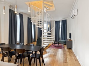 Ein modernes Wohnzimmer mit Wendeltreppe, einem Essbereich mit Holztisch und Stühlen sowie einem grauen Sofa.