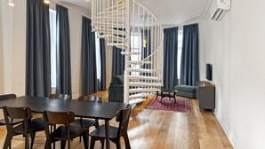 Ein modernes Wohnzimmer mit Wendeltreppe, einem Essbereich mit dunklem Holztisch und -stühlen sowie einem grauen Sofa.