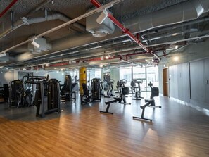 A spacious gym with various exercise equipment, large windows, and a high ceiling with visible ductwork.