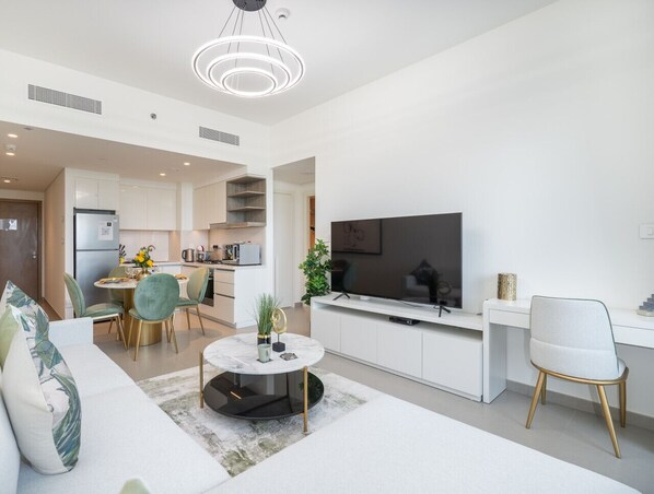 Ein modernes Wohnzimmer mit Sofa, Couchtisch und Fernseher. Im Hintergrund befindet sich ein Essbereich mit Stühlen und eine Küche.