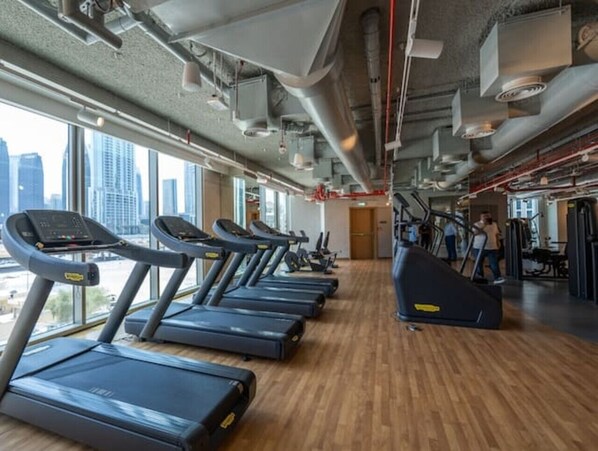 Une salle de sport équipée de tapis de course, d’une machine de musculation et offrant une vue sur les gratte-ciel de la ville grâce à de grandes fenêtres.