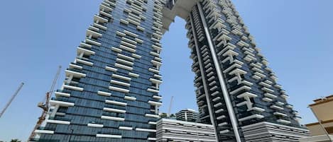 A modern high-rise building with a unique architectural design, featuring a series of balconies and a prominent overhanging structure at the top.