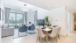 Uma sala de estar moderna com um sofá, uma mesa de jantar posta para quatro pessoas e uma janela grande com vista para a cidade.