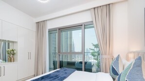 Quarto de hotel moderno com uma cama grande, varanda e vista para a cidade, além de um guarda-roupa branco.