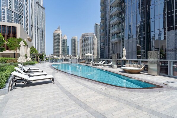 Una piscina en la azotea con sillones de descanso y una zona de estar, rodeada de edificios altos.