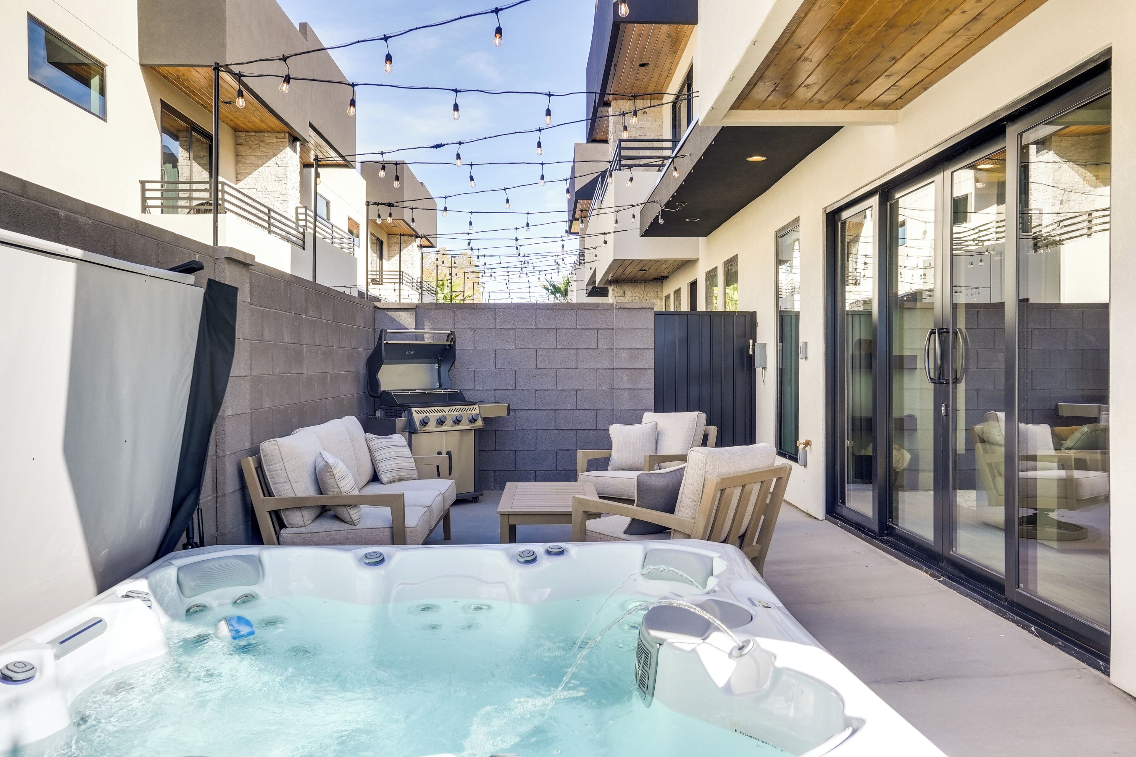 A modern outdoor patio with a hot tub, seating area, and a barbecue grill.