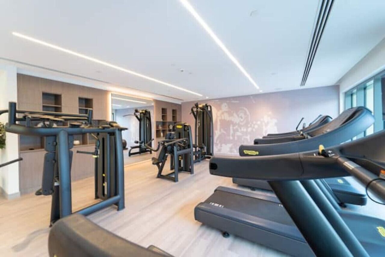 Une salle de sport moderne équipée de tapis de course, d’appareils de musculation et d’un mur entièrement recouvert de miroirs.