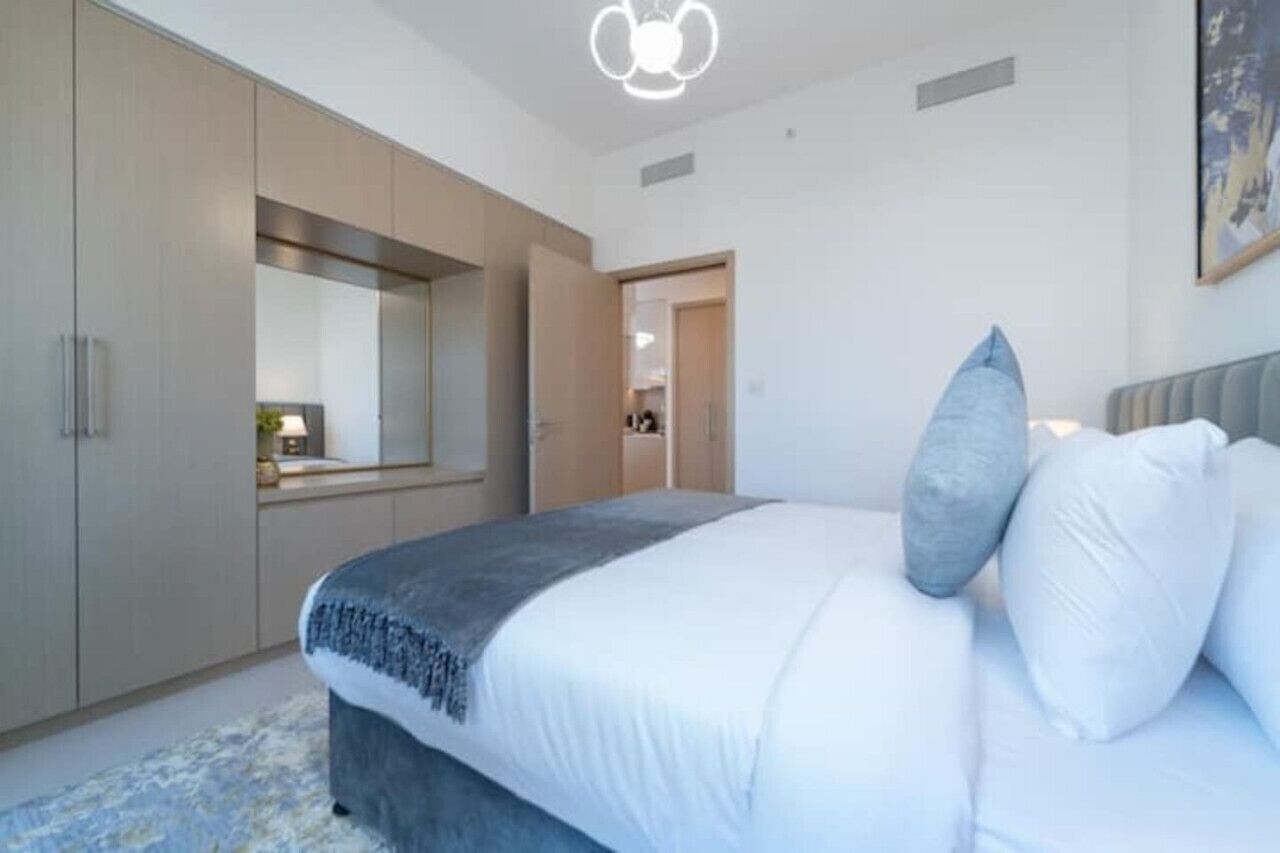 A modern bedroom with a large bed, a wardrobe, and a mirror.