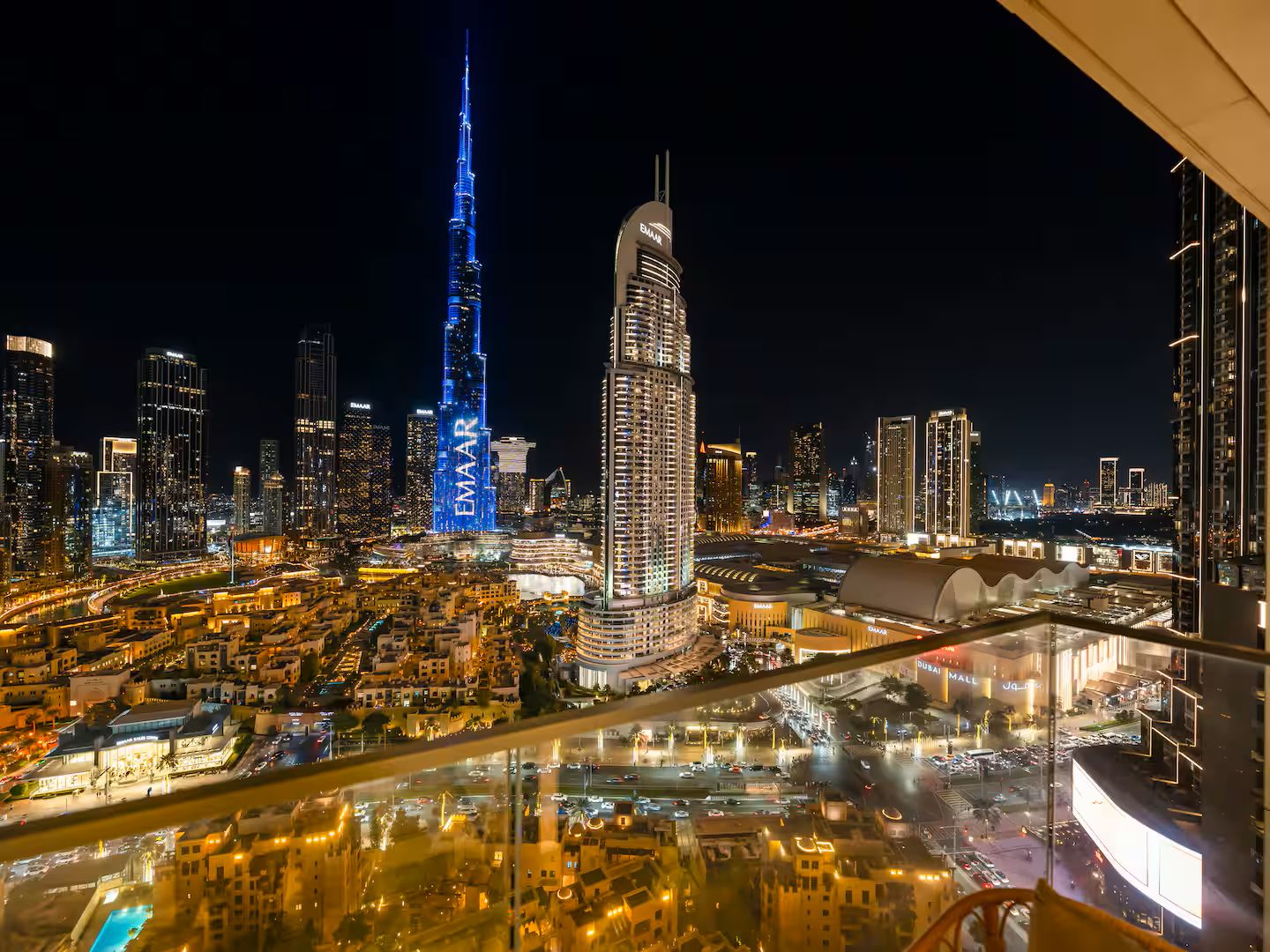 Une vue nocturne d’une ville, avec ses imposants gratte-ciel, dont le Burj Khalifa et la tour Emaar, qui se reflètent dans une étendue d’eau.