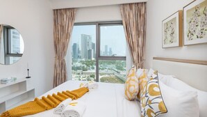 Une chambre d’hôtel avec un grand lit, une vue sur le paysage urbain par la fenêtre, et une table de chevet avec un miroir et une bougie.