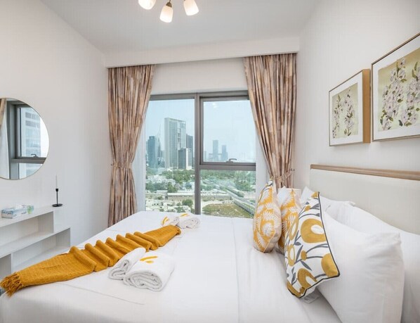 Ein Hotelzimmer mit einem großen Bett, Blick auf die Stadt durch das Fenster und einem Nachttisch mit Spiegel und Kerze.