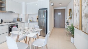 Une cuisine moderne avec des meubles blancs, un réfrigérateur en acier inoxydable et un coin repas aménagé pour quatre personnes, avec des chaises blanches.