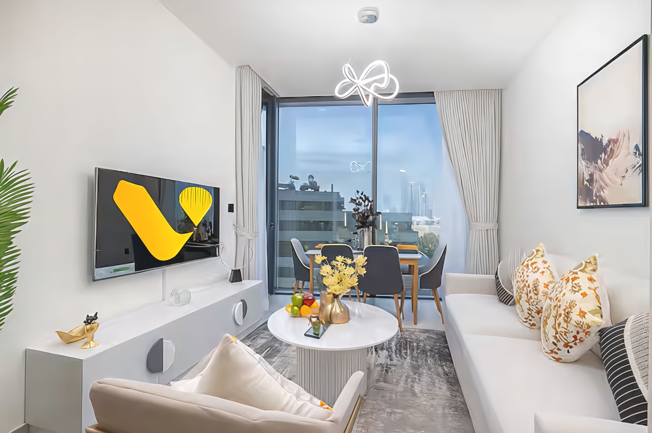 A modern living room with a flat-screen TV, a round coffee table with a vase of flowers, a sofa, and a dining area with chairs.