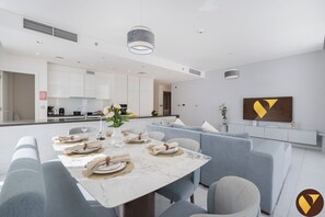 A modern dining area with a marble table set for six, light blue upholstered chairs, and a contemporary kitchen in the background.